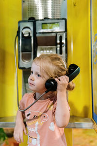 Little girl pretend talking on a retro wire phone on street