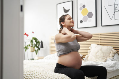 Pregnant woman sitting on bed at home