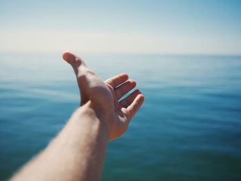 Cropped image of hand against sea