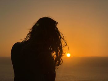 Silhouette woman standing by sea during sunset