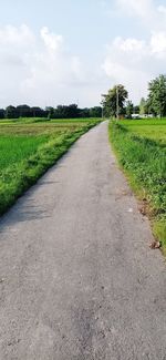 Empty road amidst field against sky