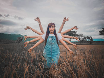 Young woman with arms raised standing on field against sky
