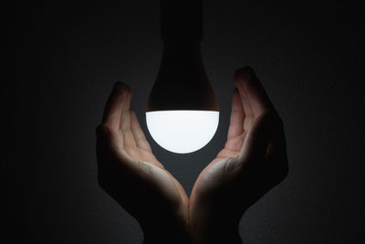 Close-up of hand holding illuminated lamp against black background