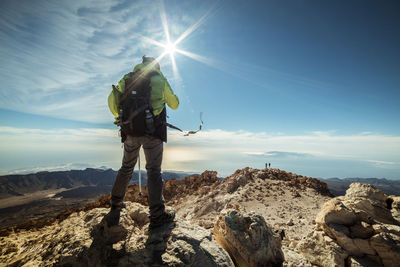 Rear view of hiker standing on mountain against sky