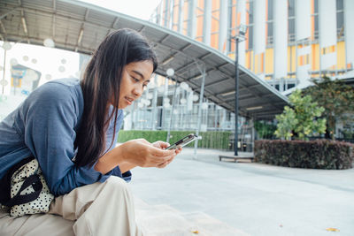 Young woman using mobile phone on street in city