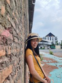 Portrait of beautiful woman standing against brick wall