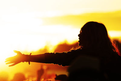 Silhouette woman with arms raised against sky during sunset