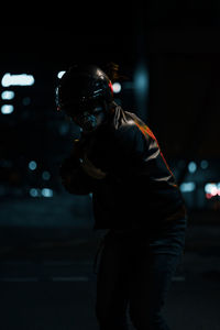 Side view of man in leather jacket preparing to swing a bat standing on a street at night