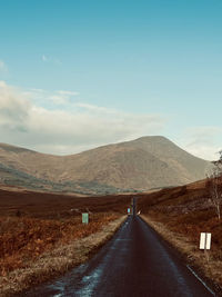 Empty road leading towards mountains against sky