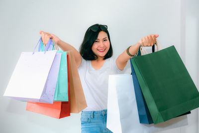 Portrait of woman holding shopping bags against wall