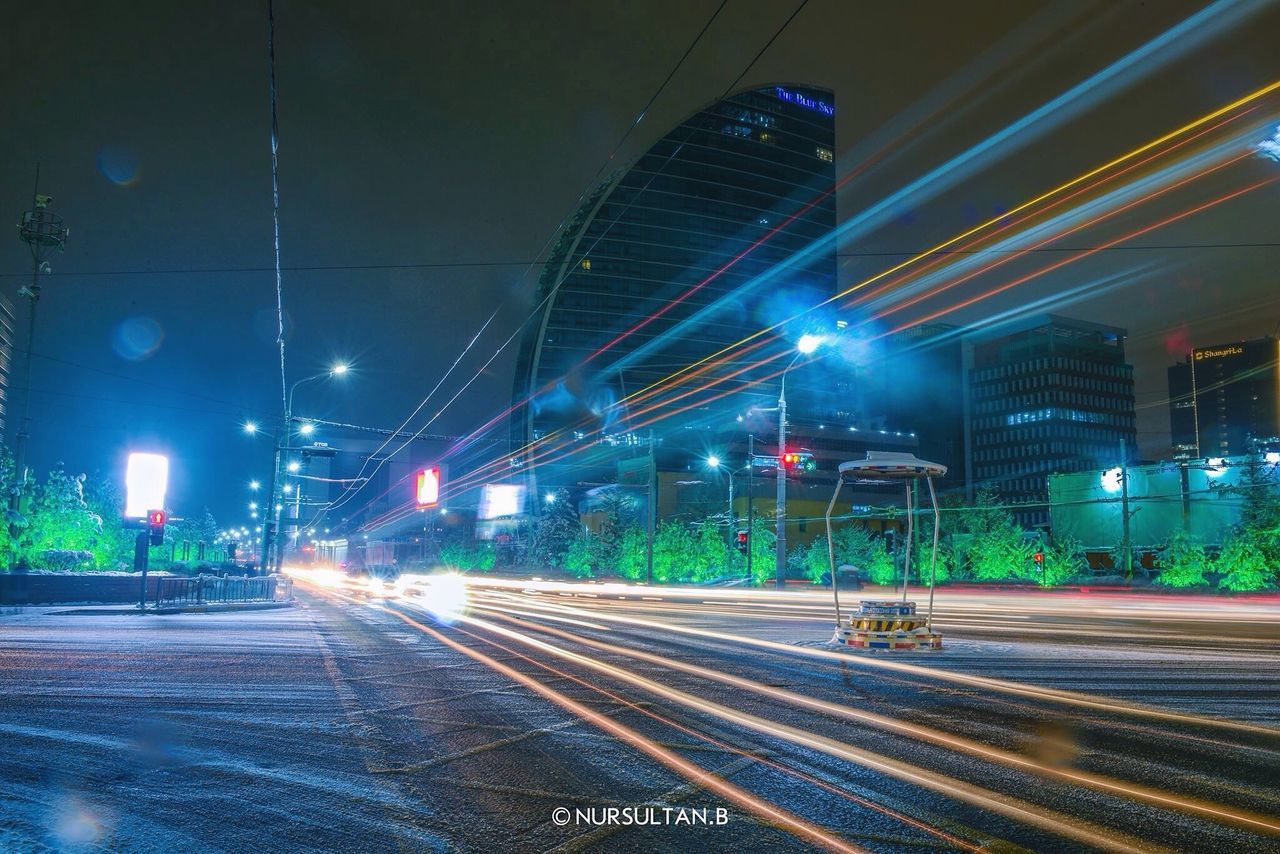 illuminated, night, long exposure, light trail, motion, speed, transportation, blurred motion, city life, street light, city, street, outdoors, building exterior, road, built structure, architecture, no people, high street, urban scene, sky