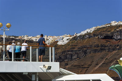 Rear view of men standing on mountain against clear blue sky