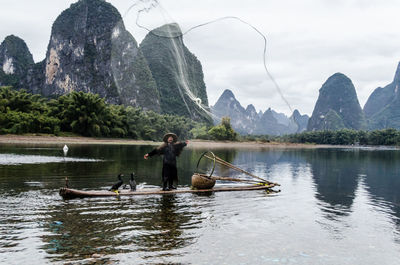 Rear view of men fishing in lake against sky