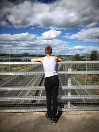 Rear view of woman standing on railing against sky