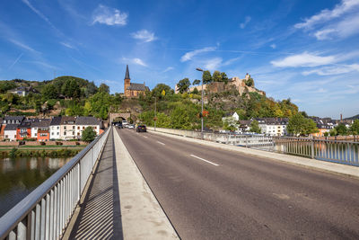 Bridge over river by buildings in city against sky