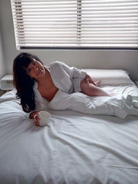 Portrait of seductive woman holding mug lying on bed