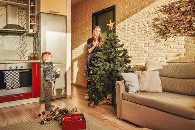 Boy looking at mother decorating christmas tree