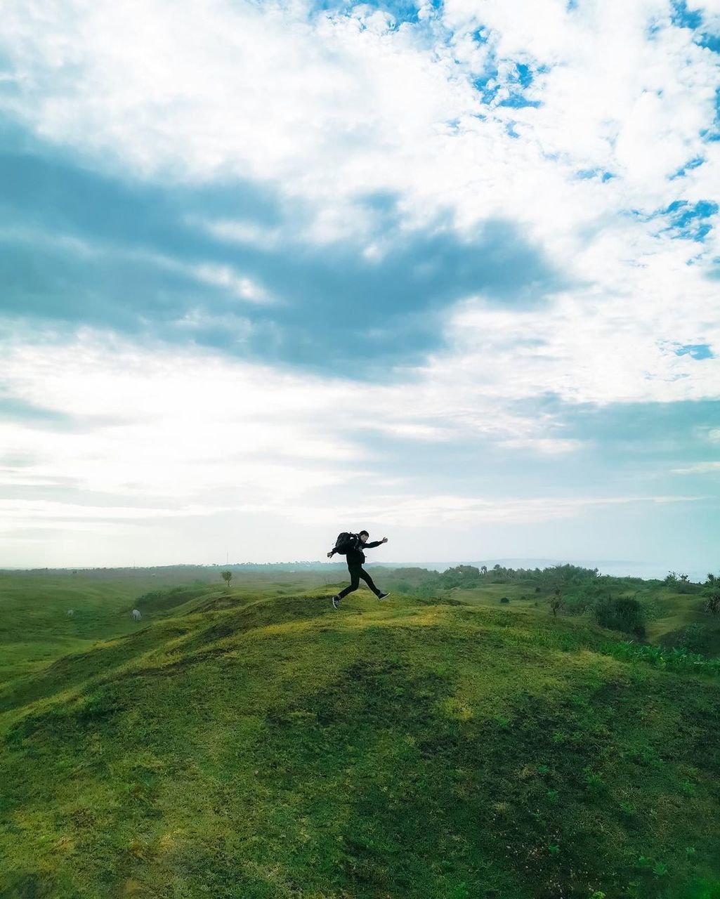 sky, hill, cloud, grass, one person, landscape, nature, environment, grassland, leisure activity, horizon, full length, land, plant, rural area, meadow, activity, scenics - nature, beauty in nature, green, sports, adult, day, tree, field, non-urban scene, outdoors, lifestyles, men, tranquility, plain, tranquil scene, standing, terrain, rural scene, sunlight, travel, recreation, vacation, sea, trip, holiday, prairie