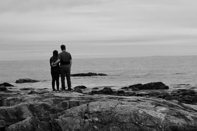 Rear view of friends standing on rock by sea against sky