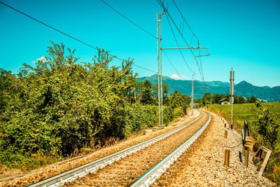 Railroad tracks by trees against blue sky