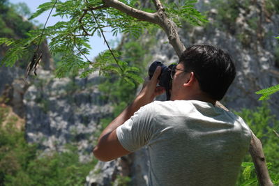 Rear view of man photographing through digital camera in forest