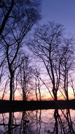 Silhouette bare trees by lake against sky at sunset