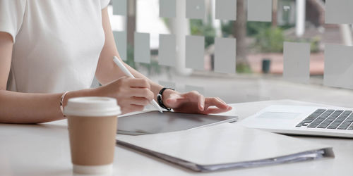 Midsection of woman holding smart phone while sitting on table