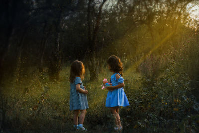 Side view of girls standing on field during sunset