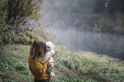 A woman is holding a baby near a river