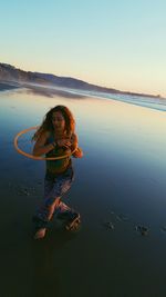 Portrait of young woman standing at beach against clear sky