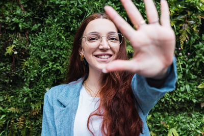 Portrait of smiling woman with long red hair pulling hand towards camera. beautiful woman having fun