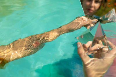 Reflection of woman in mirror holding prism while sitting in swimming pool