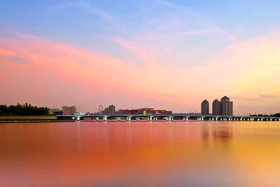 Scenic view of lake by illuminated buildings against sky during sunset