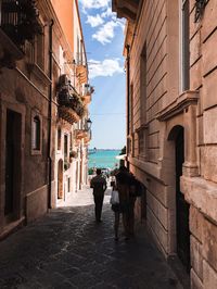 Rear view of people walking on alley amidst buildings in city