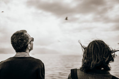 Rear view of people at sea shore against sky