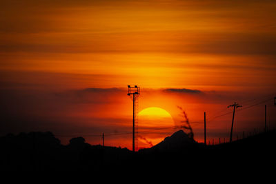 Silhouette of electricity pylon against orange sky