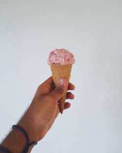 Close-up of hand holding ice cream against white background