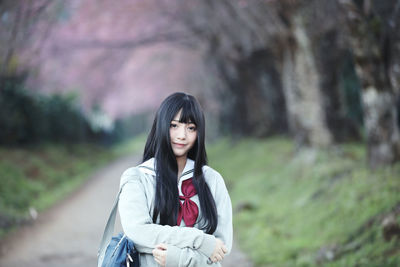 Portrait of young woman standing against trees