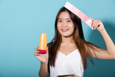 Portrait of young woman holding ice cream against blue background