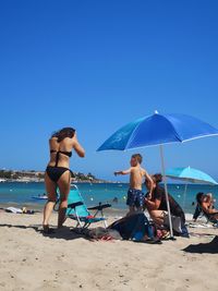 Friends on beach against clear blue sky