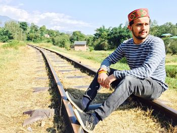 Man sitting on railroad track against sky