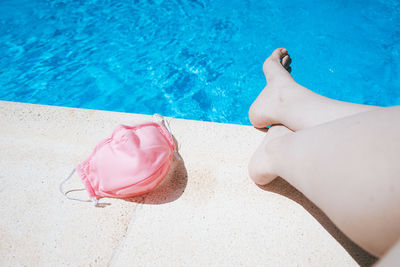 Low section of woman with mask sitting at poolside