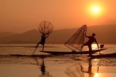 Fishermen fishing in lake against sky during sunset