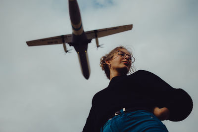 Low section of woman standing against airplane flying in sky