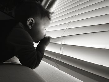 Tilt image of curious boy peeking through blinds at home