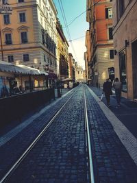 Rear view of people walking on railroad track in city