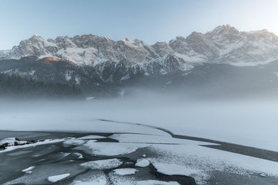 Scenic view of frozen lake by mountains against sky during foggy weather