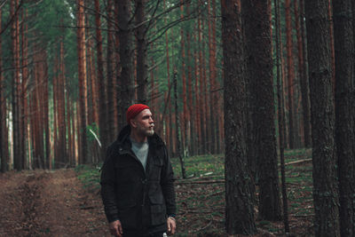 Man standing by tree trunk in forest