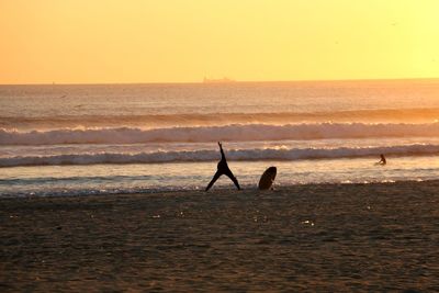 Person exercising at beach against sky during sunset