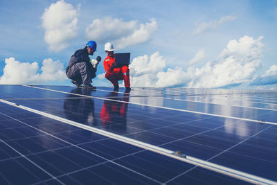 Low angle view of male technicians working on solar panels against sky